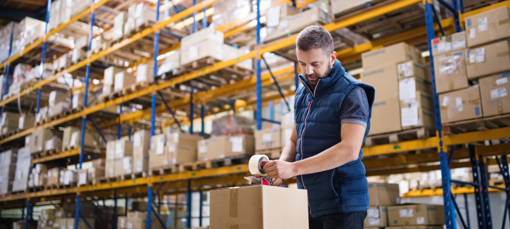 male warehouse worker sealing cardboard boxes