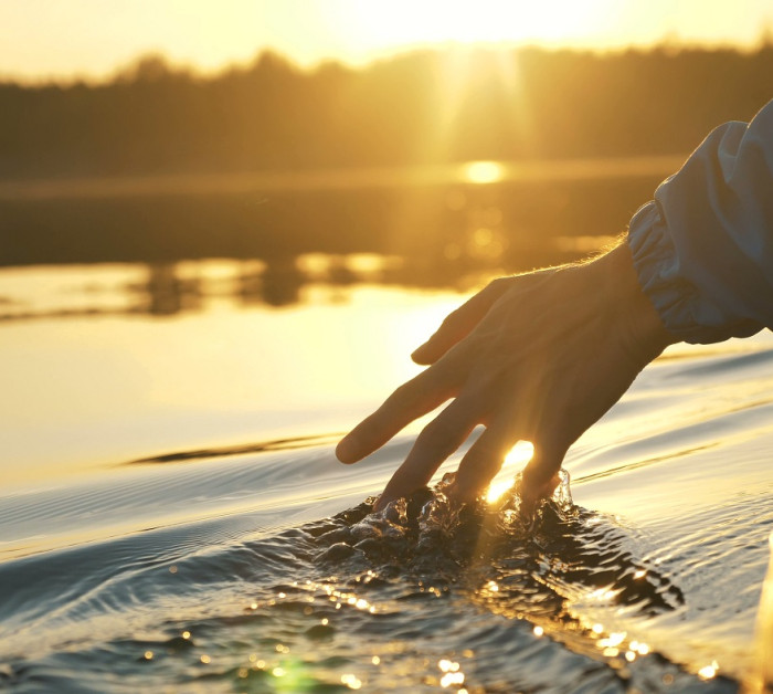man puts fingers down lake kayaking