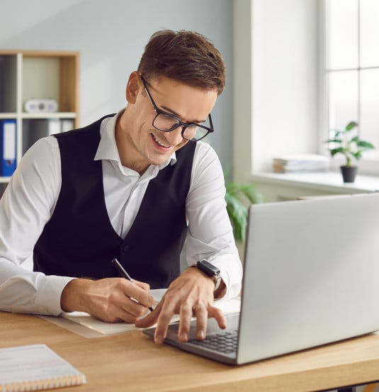 Man writing in notebook with laptop